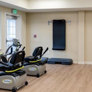 A gym room featuring two stationary bikes and wall-mounted exercise equipment.