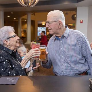 An elderly couple enjoying a drink and sharing smiles in a lively restaurant setting.
