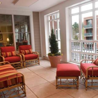 A sunlit seating area with comfortable chairs and ottomans near large windows.