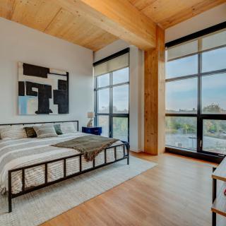 A modern, minimalist bedroom with large windows and wooden flooring, featuring a stylish bed and contemporary artwork.