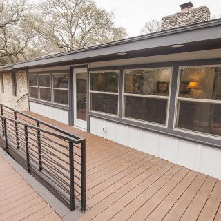 A view of a house with a spacious deck and railing, featuring large windows and surrounded by trees.