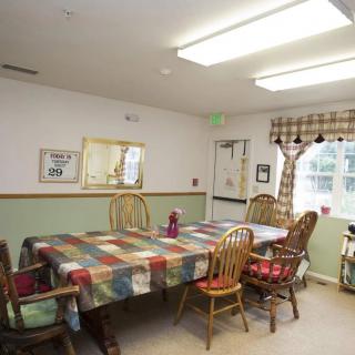 A cozy dining room with a plaid tablecloth covering the table, surrounded by wooden chairs and natural light coming through the window.