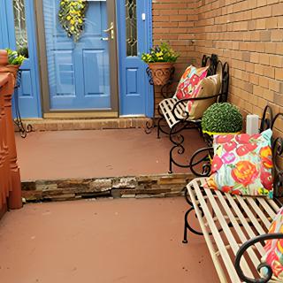 A welcoming front porch with blue doors, adorned with colorful pillows on benches and potted plants.