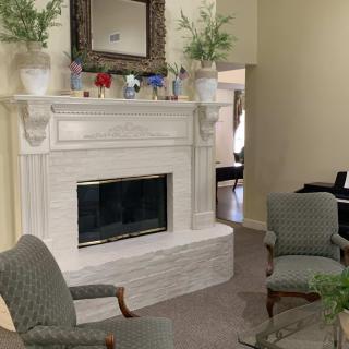 A cozy living room featuring a white fireplace adorned with decorative plants and surrounded by comfortable chairs.