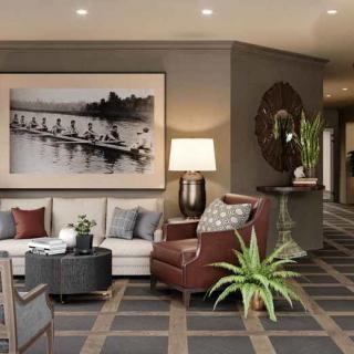 A cozy living room featuring a sofa, armchair, coffee table, large artwork on the wall, and decorative plants.