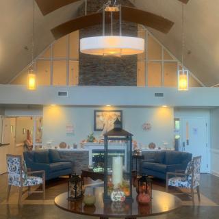 A modern living room with high ceilings, featuring a central chandelier, two blue sofas, and a round coffee table adorned with decorative items.