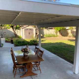 A covered patio with a dining table set and chairs, overlooking a backyard garden.