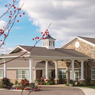 A charming community center with a blend of stone and modern architecture, surrounded by trees under a partly cloudy sky.