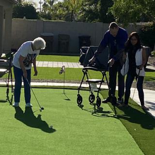 A senior woman enjoys a game of golf with the assistance of family members, showcasing a leisurely day outdoors.