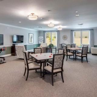 A spacious dining area with multiple tables and chairs, featuring a television and large windows.