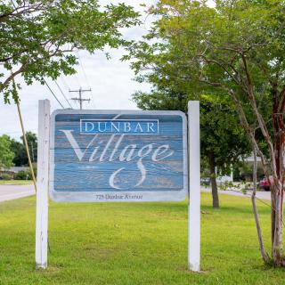 A wooden sign for Dunbar Village standing beside a grassy area with trees.