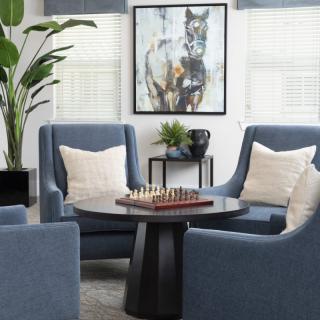 A modern living room with blue armchairs, a chess board on the table, and wall art creating a cozy atmosphere.