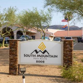 A sign for South Mountain with a building and mountains in the background.