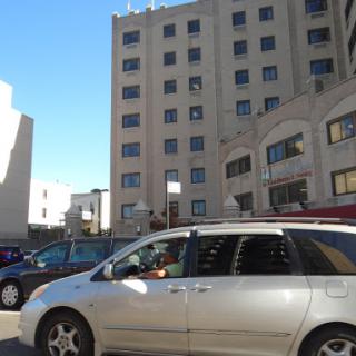 A view of a city street featuring parked cars and buildings under a clear sky.