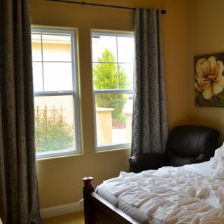 A cozy bedroom with a bed, armchair, and large windows letting in natural light.