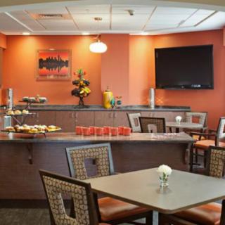 A modern restaurant interior showcasing neatly arranged tables and chairs, with a buffet counter in the background.