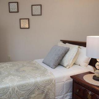 A cozy bedroom featuring a neatly made bed with pillows and a nightstand with a lamp.
