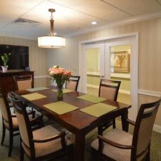 A cozy dining room with a wooden table, chairs, and a vase of flowers under warm lighting.
