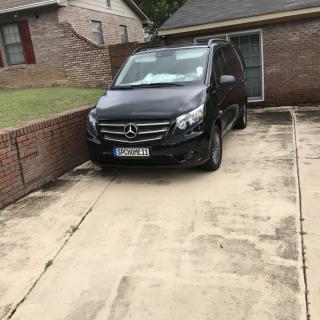 A black Mercedes-Benz van parked in a driveway next to a brick wall and house.