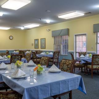 A well-arranged dining room with tables set for a meal, featuring floral centerpieces and neatly folded napkins.