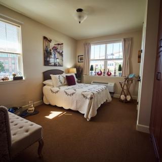 A cozy bedroom with a neatly made bed and ample natural light from two windows.