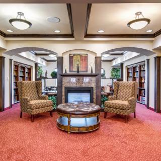 A cozy library with a central fireplace, surrounded by armchairs and bookshelves.