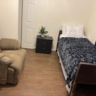 A simple bedroom with a single bed, nightstand, and recliner chair.