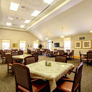 Spacious dining area with multiple tables and chairs, well-lit by ceiling lights and natural light from windows.