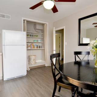 A modern kitchen dining area featuring a round black table with chairs, an open pantry, and a white refrigerator.
