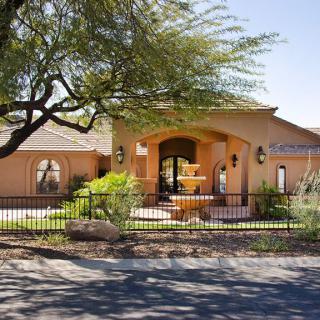 A beautiful residential home with a fountain and gated entry, surrounded by landscaped greenery.