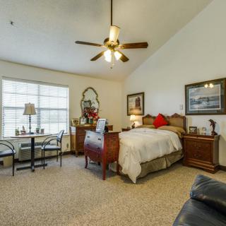 A cozy bedroom featuring a bed, dresser, and a window with curtains, complemented by a ceiling fan and decorative furnishings.