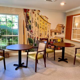 A cozy indoor seating area with tables and chairs, featuring a mural and a large window.