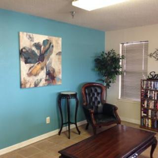 A cozy office corner with a leather chair, abstract painting, and bookshelf.