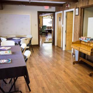 A meeting room with tables and chairs, featuring a whiteboard and wood floors.