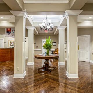 A well-lit lobby area with elegant columns and a central table featuring decorative plants.