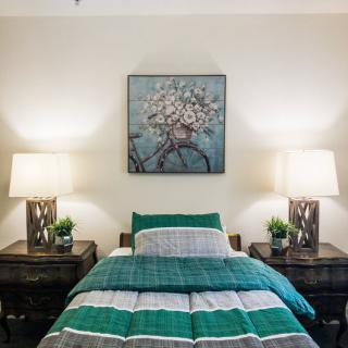 A cozy bedroom with a neatly made bed, flanked by nightstands and lamps, complemented by a floral artwork above the headboard.