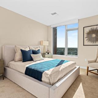A cozy modern bedroom featuring a comfortable bed with stylish blue accents and ample natural light from the large window.