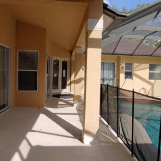 A covered patio area next to a screened-in pool at a residential home.