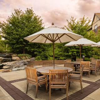 A cozy outdoor patio with wooden furniture and umbrellas surrounded by lush greenery.