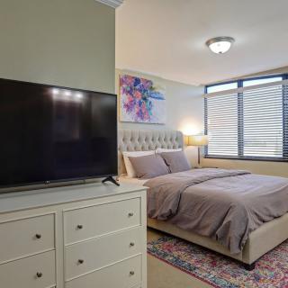 A cozy bedroom featuring a large bed, a TV on top of a dresser, and colorful artwork over the bed adjacent to a window.
