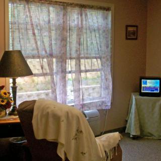 A cozy living room with a large window, sheer curtains, and a small television.