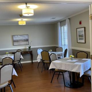 A cozy dining room with neatly arranged tables and chairs, decorated with paintings and bright lighting.