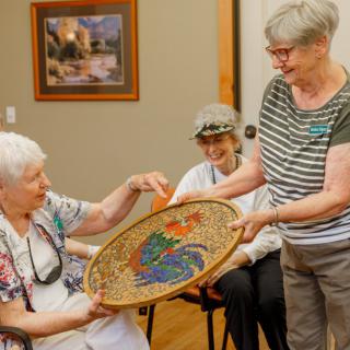 Elderly women sharing and admiring a colorful basket in an indoor setting.