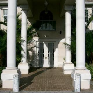 Elegant building entrance with white columns and palm trees.