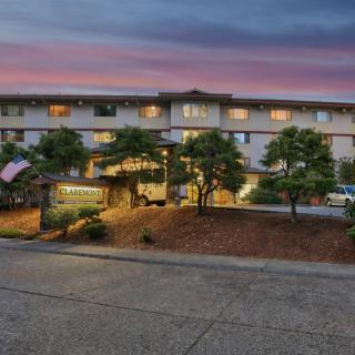 An apartment building at sunset with illuminated windows and trees in the foreground.