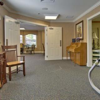 A well-lit hallway with a bench, piano, and open doors leading to a seating area.