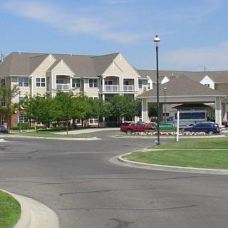 A suburban residential building with a parking lot and cars, surrounded by greenery.