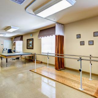 A well-lit physical therapy room featuring a ballet bar and an exercise table, designed for rehabilitation activities.