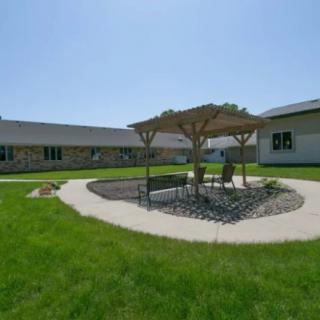 A sunny courtyard with a gazebo and outdoor seating surrounded by green grass and buildings.