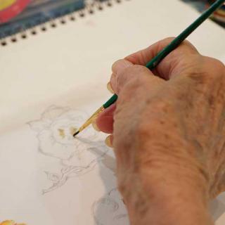 An artist's hand drawing in a sketchbook with a paintbrush.